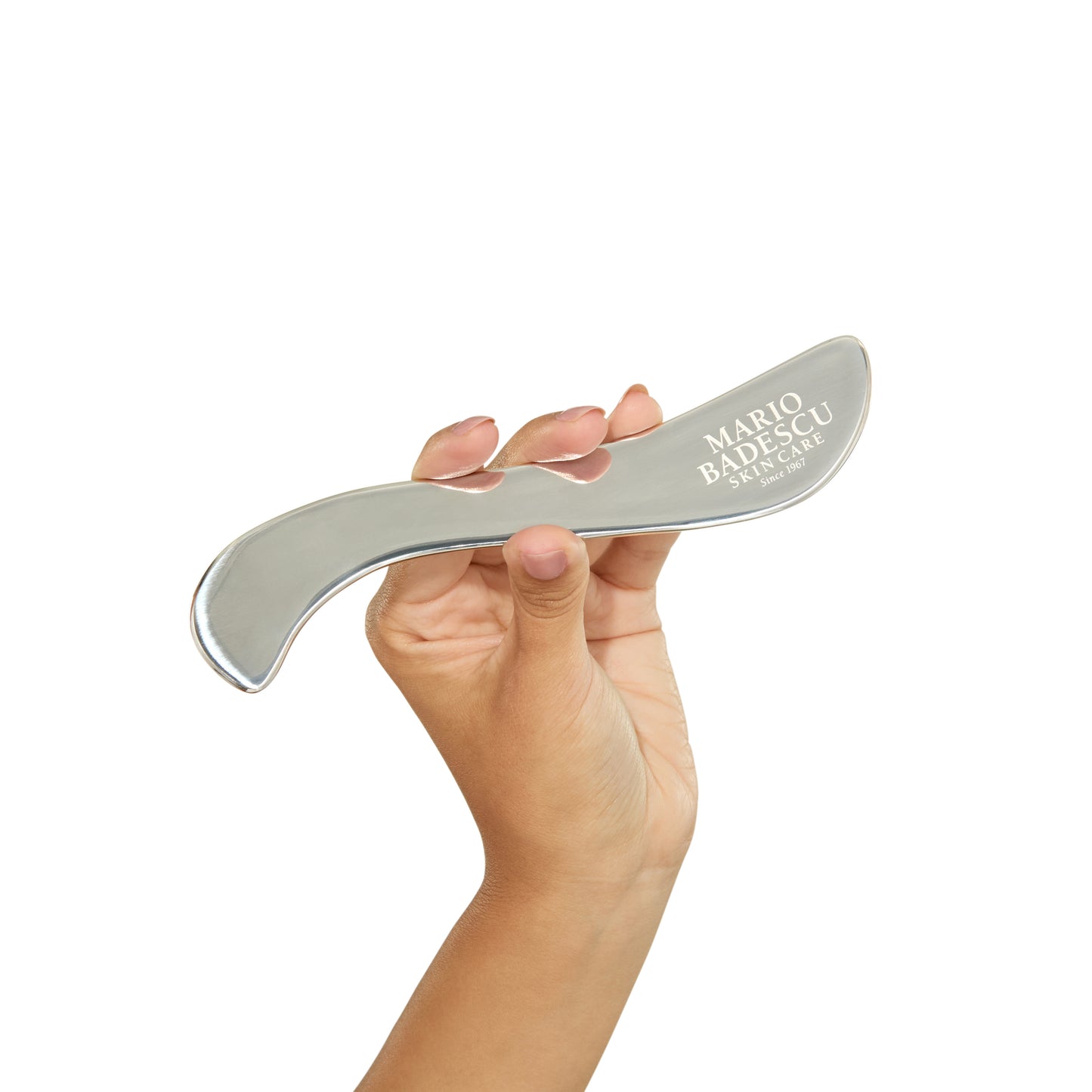 Hand holding a silver skincare tool with 'Mario Badescu' branding on a white background