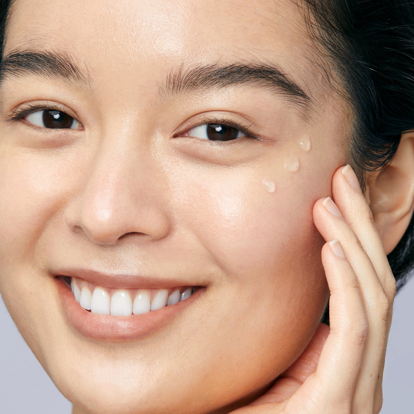 Woman with dewy skin demonstrating how to apply Hyaluronic Dew Drops